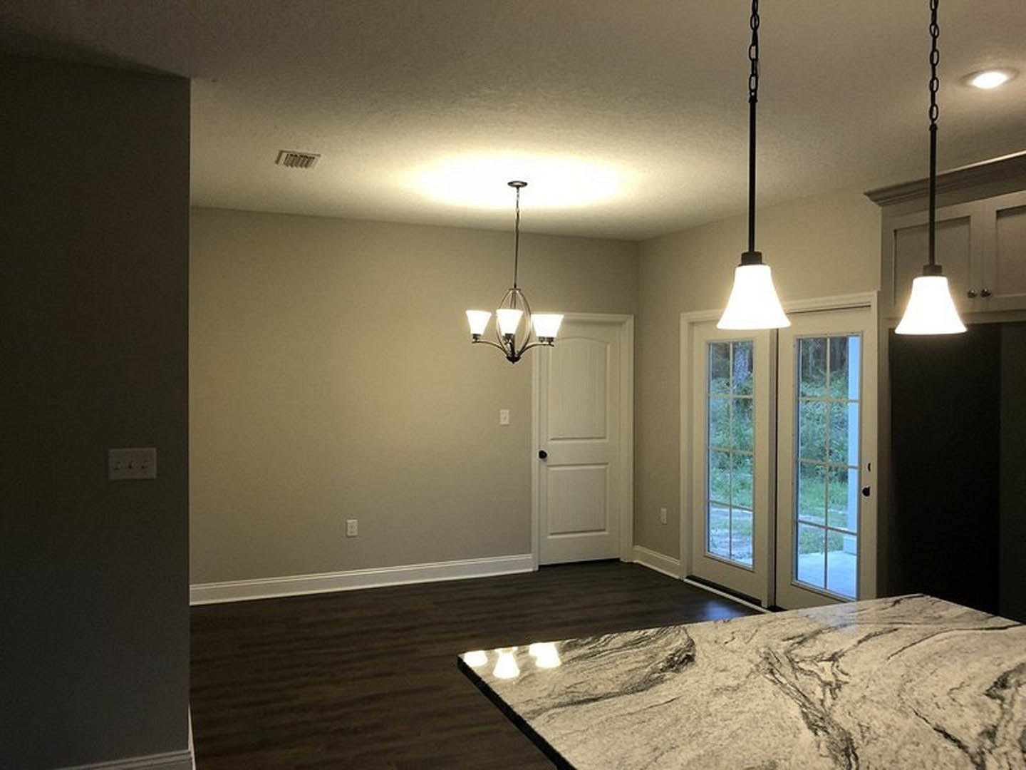 Marble countertop kitchen with double glass-paneled doors, ceiling light fixture, light switch on plaster wall, and hardwood flooring
