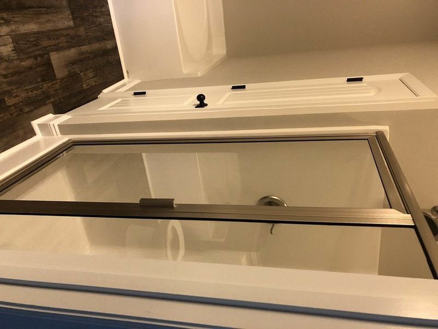 Walk-in shower with clear glass door, white tile walls, adjacent freestanding bathtub, wood accent wall with white trim, chrome fixtures, and nearby toilet.