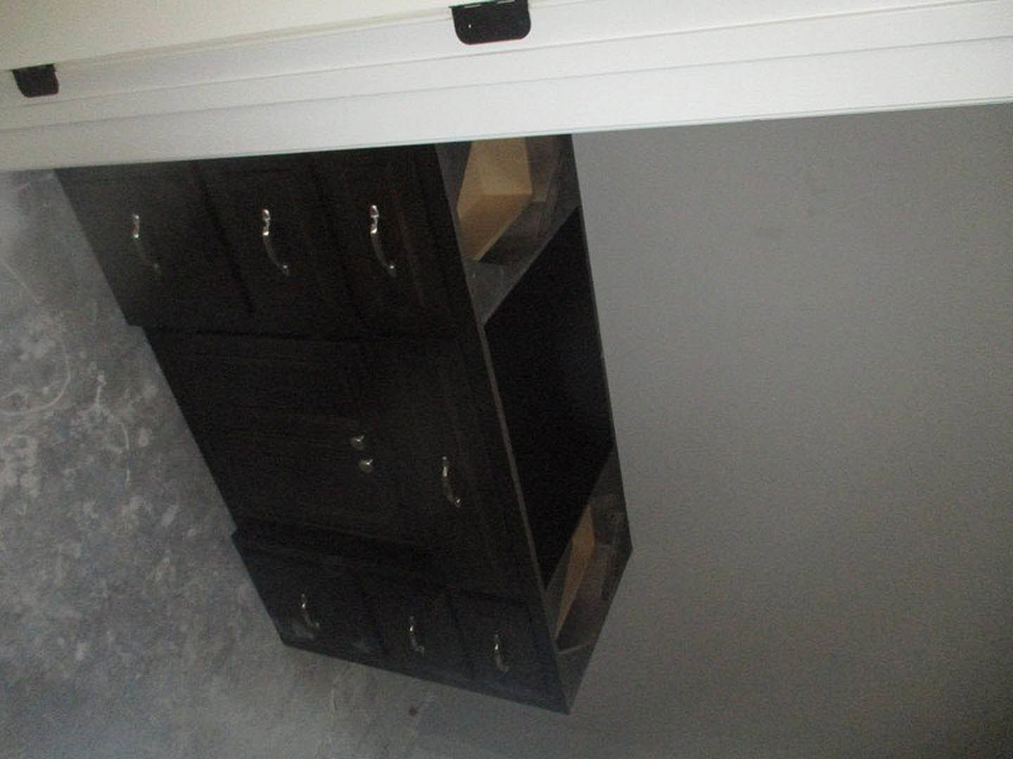 Black cabinet drawer with silver handles installed beneath a white interior door, set against a white wall with black trim.