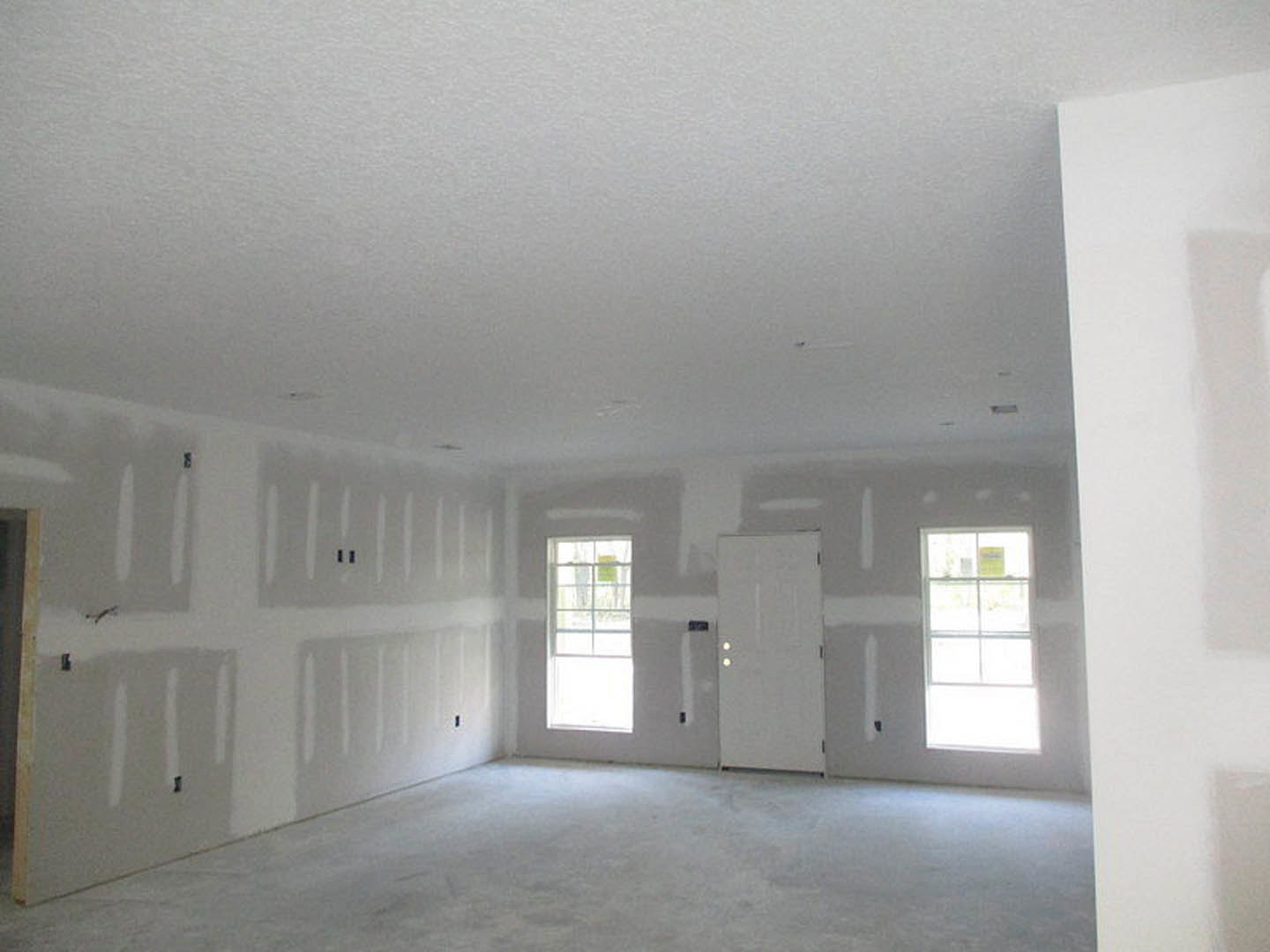 White carpeted room with white plaster walls, white framed window letting in natural light, and white paneled door.