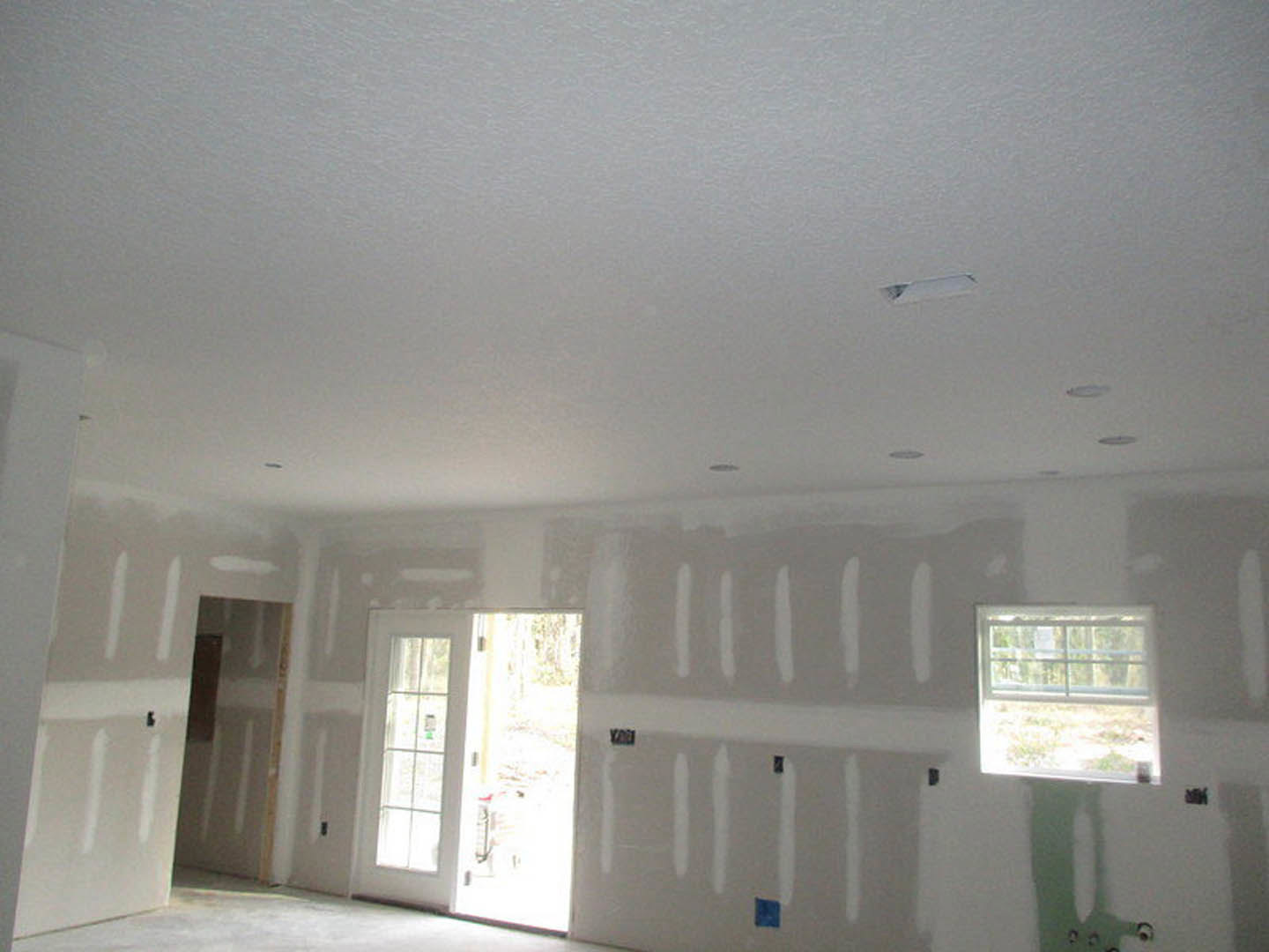 Bright room with smooth white plaster walls, large windows with white frames, white door featuring glass panes, and ceiling with recessed lighting fixtures