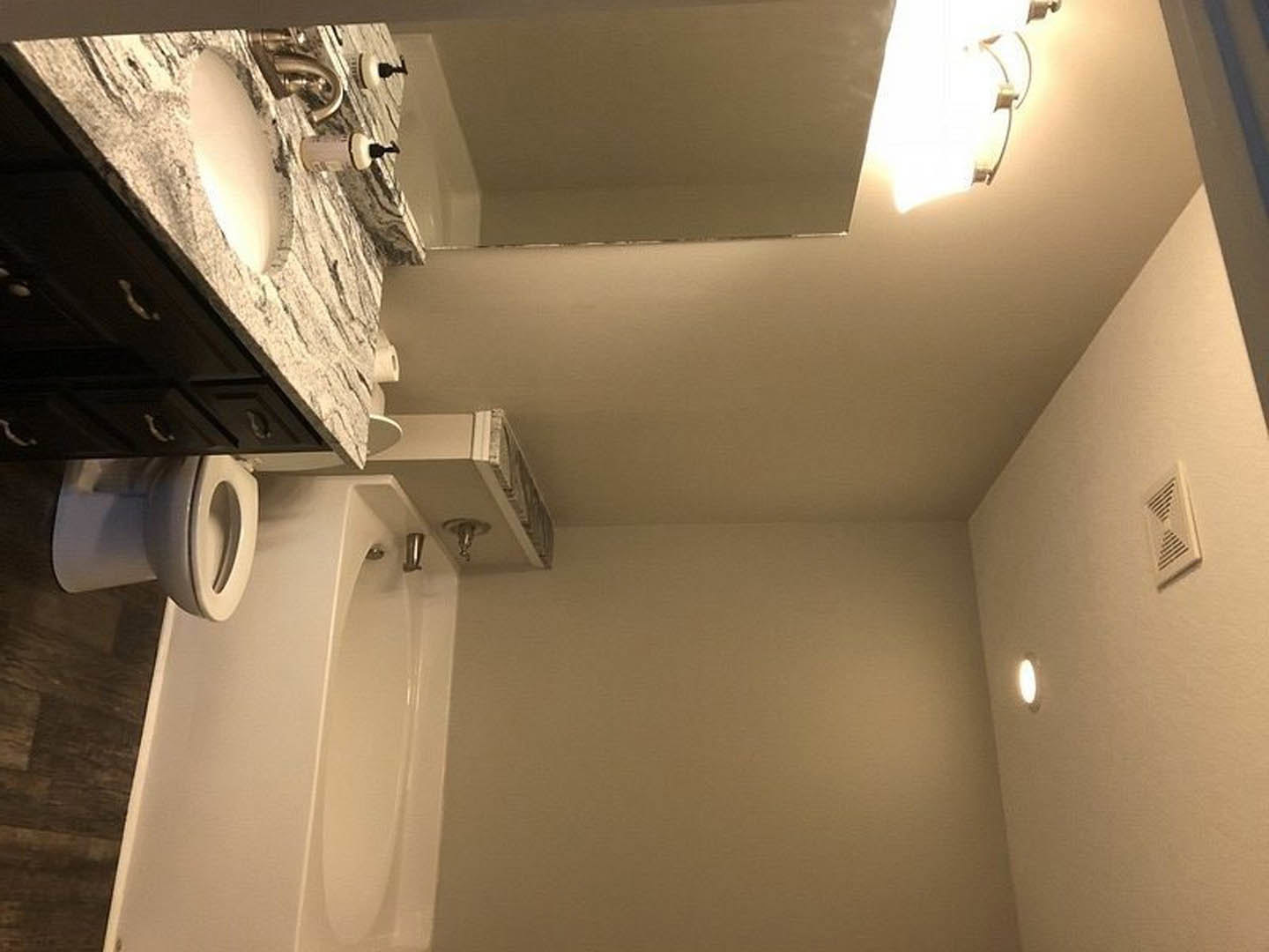 Modern bathroom featuring a white bathtub, rectangular sink with chrome faucet atop a black vanity, plaster walls, ceiling light fixture, and wall vent.