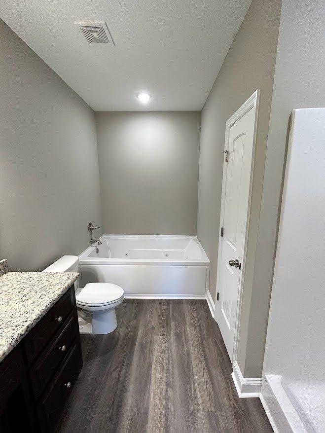 Bathroom with white toilet and bathtub, black drawer under countertop, wood flooring, light tile walls