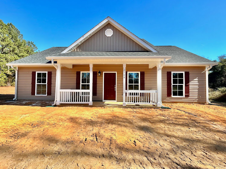Red front door and white porch railing on a house with white trim windows, gray siding, and a dirt yard.