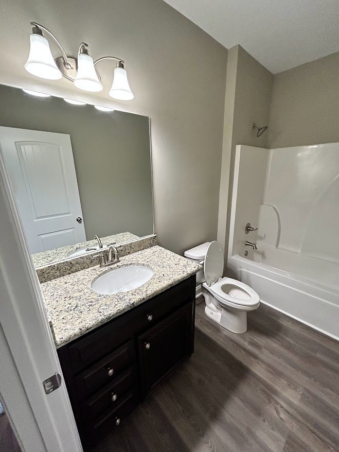 Bathroom with marble countertop, white sink, wall-mounted mirror, and toilet with lid up; light tile flooring and cabinetry visible.