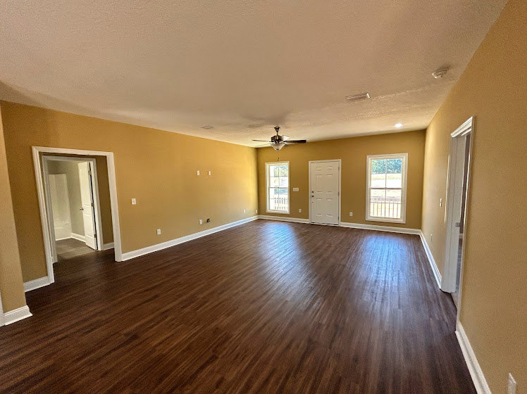 Spacious room with hardwood flooring, neutral walls, and ceiling fan centered above.