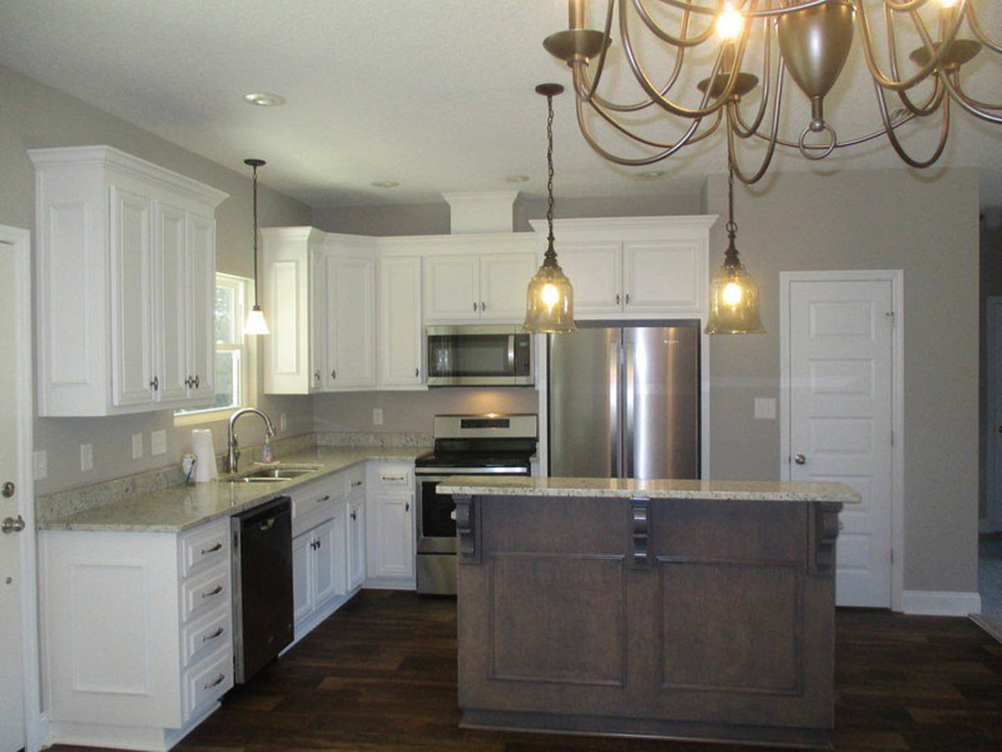 White kitchen with shaker cabinets, large central island with quartz countertop, stainless steel appliances, pendant lighting, and farmhouse sink