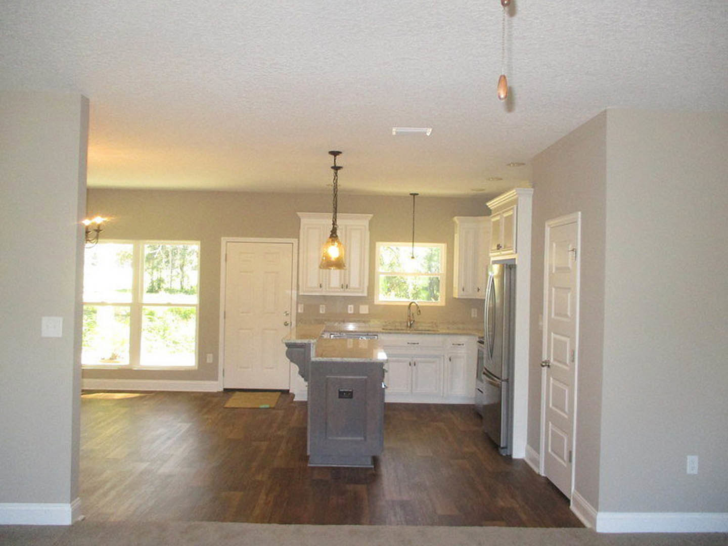 Kitchen with stainless steel refrigerator, white cabinetry, central island with stone countertop, light walls, and wood flooring