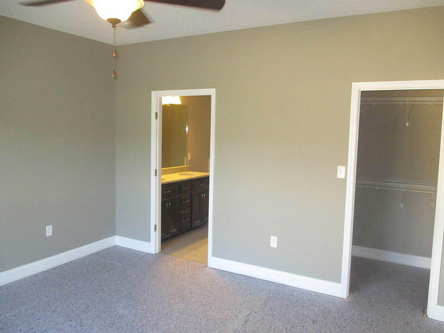 Bathroom with white framed door open, single sink vanity, wall mirror, light-colored walls, carpeted floor, and ceiling fan visible