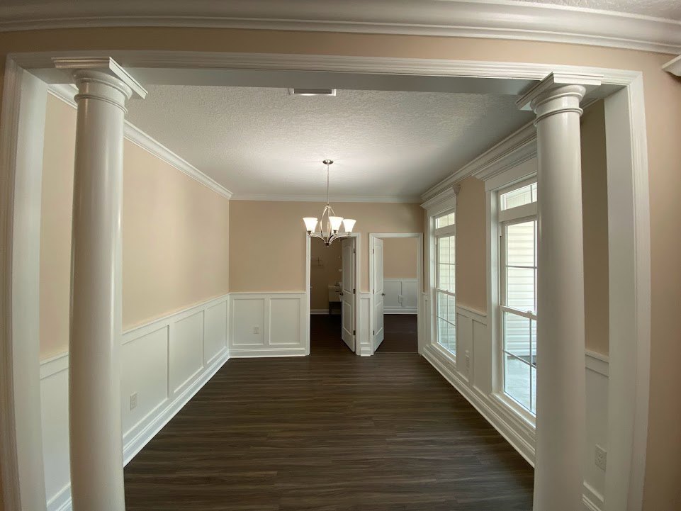 Hallway with dark wood flooring, white columns, white doors, and a chandelier with three lights hanging from the ceiling