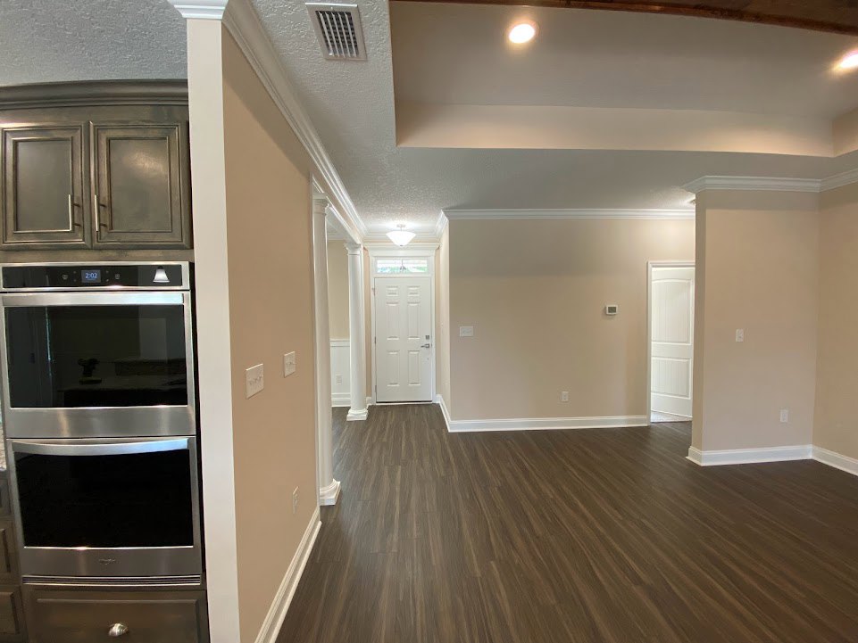 Kitchen with wood plank flooring, white cabinetry, stainless steel stove, built-in microwave, and white paneled door with silver handle