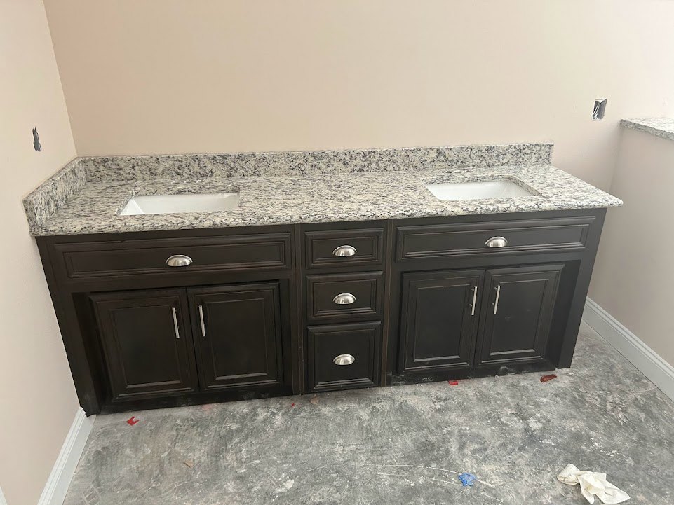 Granite bathroom vanity countertop with black and white speckled surface, white cabinetry, drawers, and chrome faucet
