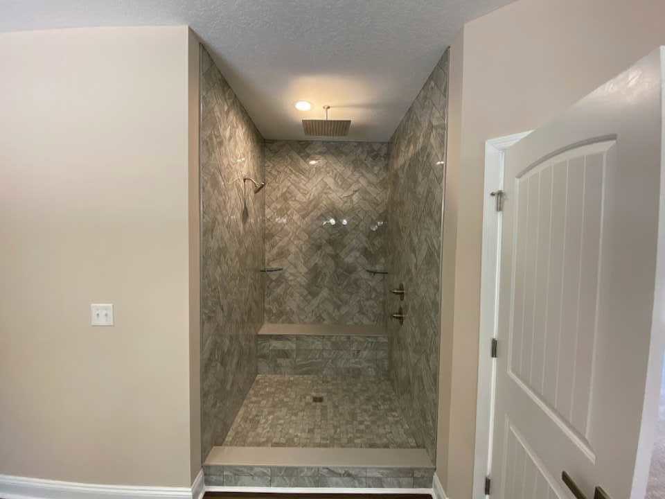 Walk-in shower with marble tile floor, white plaster walls, glass door, and chrome fixtures in modern bathroom