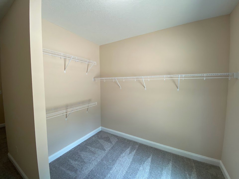 Walk-in closet with white built-in shelves, white metal hanging rod, carpeted floor, and smooth white ceiling
