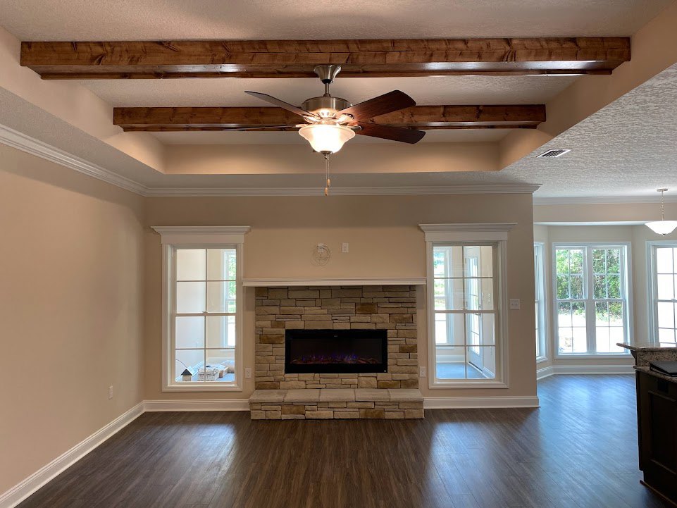 Living room with hardwood flooring, stone accent wall featuring a black rectangular fireplace with blue lights, ceiling fan, multi-pane window, and glass-paneled door.