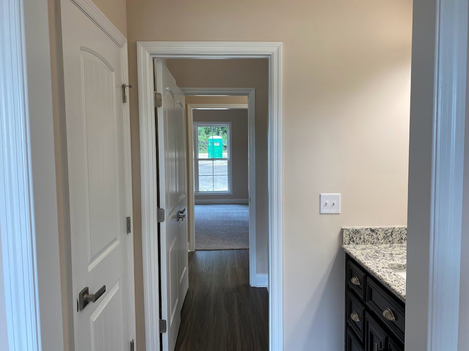Hallway featuring marble countertop sink, white cabinetry, carpeted floor, white-framed window, green potty, and dual-knob light switch