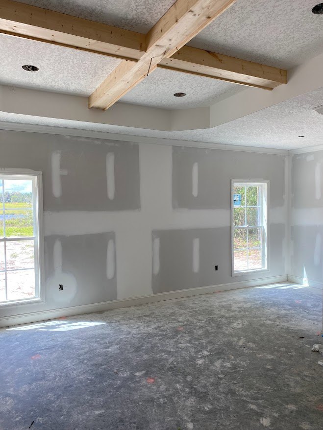 White plaster walls, large windows with white frames overlooking grass and trees, exposed wooden ceiling beams