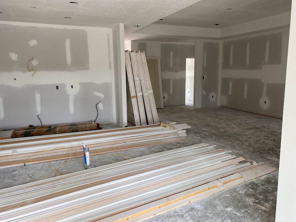 White-painted walls and ceiling, light wood plank flooring, natural wood planks stacked near a wall, glass jar with paintbrush, cardboard box on the floor.
