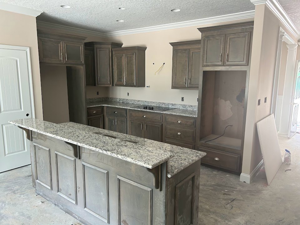 Modern kitchen featuring light-colored countertops, white cabinetry, stainless steel sink, and built-in appliances; white door with hardware and visible wiring near a grey