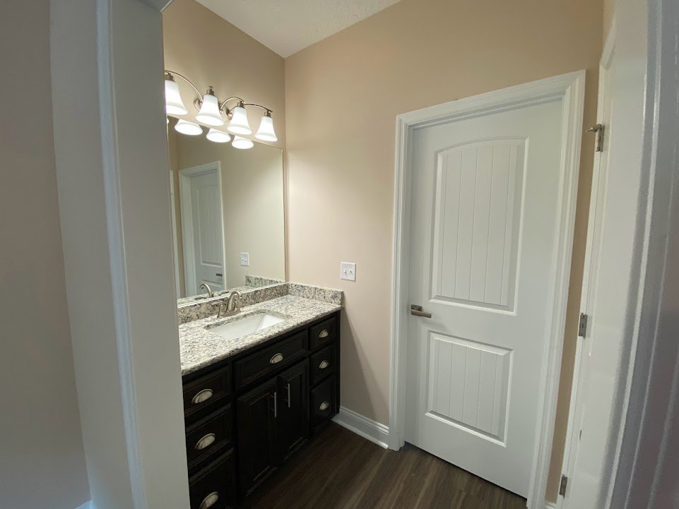Bathroom with marble countertop sink, white cabinetry, silver faucet, row of ceiling lights, and white door with silver handle