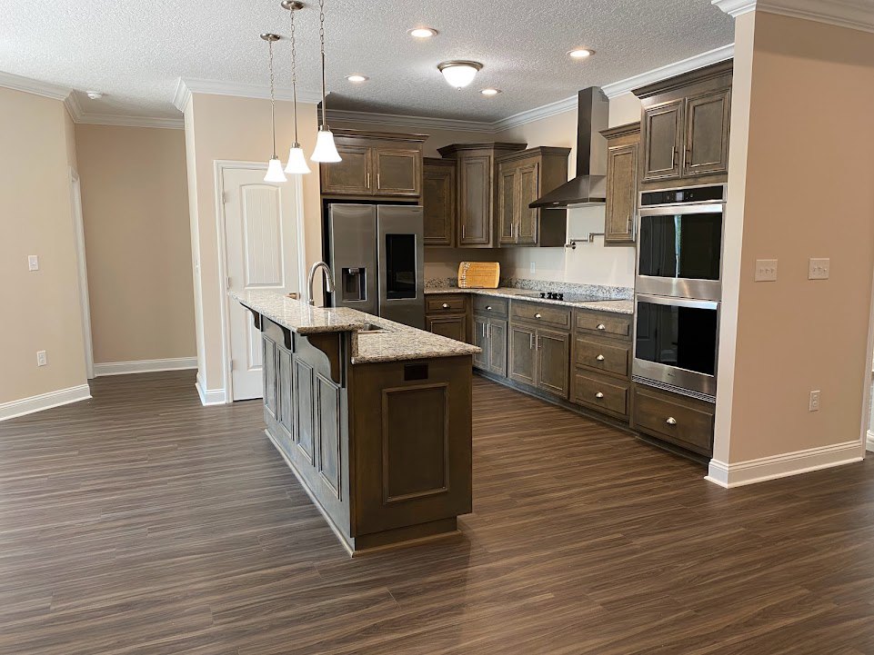 Kitchen with wood flooring, white cabinetry, stainless steel refrigerator and microwave, granite-topped island, pendant light fixture, and a close-up of a door.