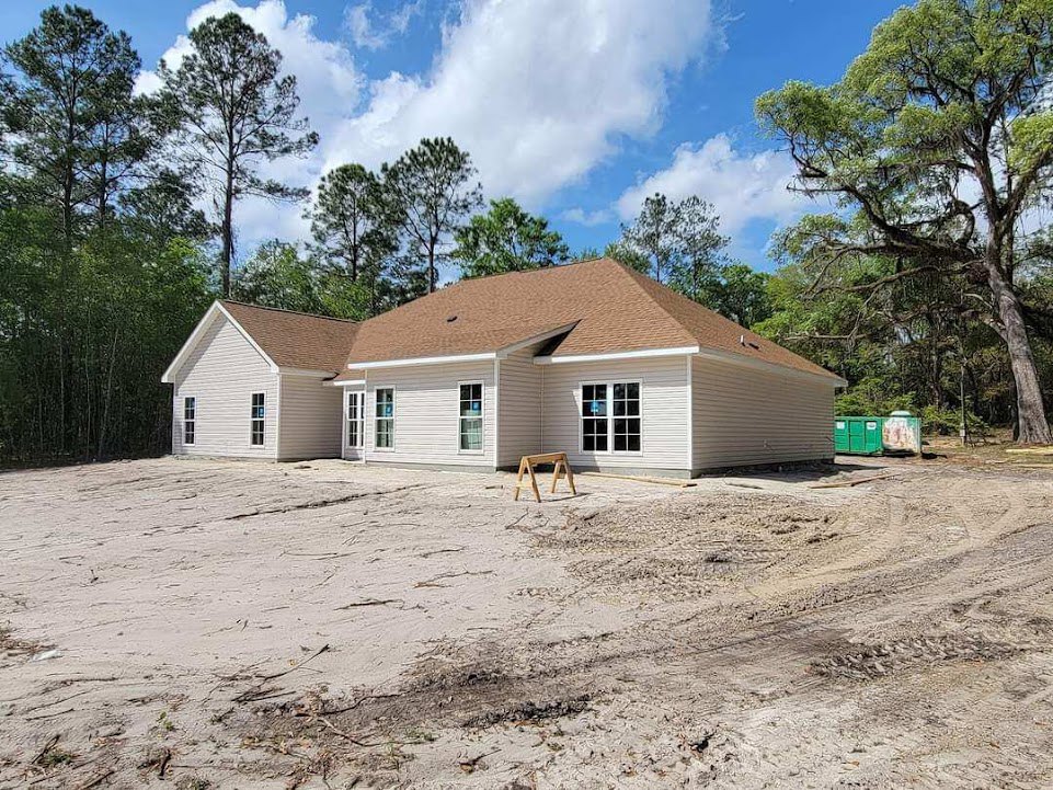 Partially built wooden house with brown roof surrounded by trees, dirt construction area in foreground, Canyon Lake and blue sky with clouds in background