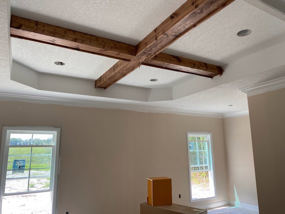 Living room with exposed wooden ceiling beams, plaster walls, white-framed windows, and a ceiling fan fixture.