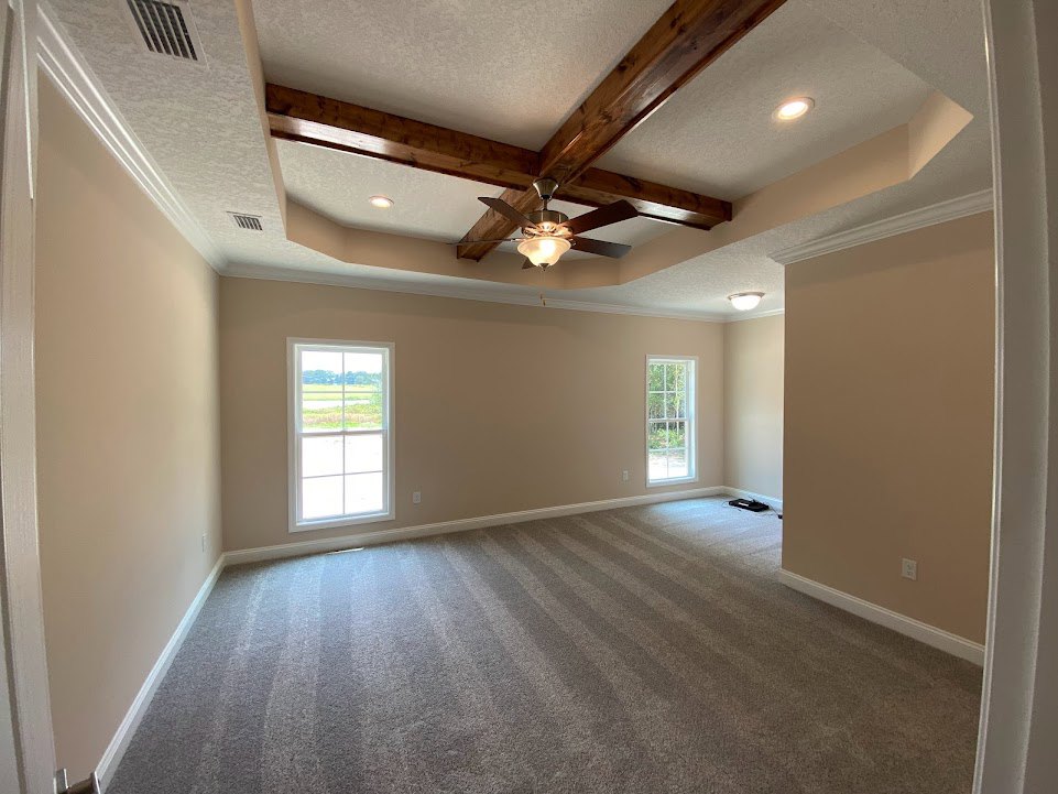 Carpeted room with striped flooring, white-framed windows overlooking a field, ceiling fan, plaster walls, and wall vent
