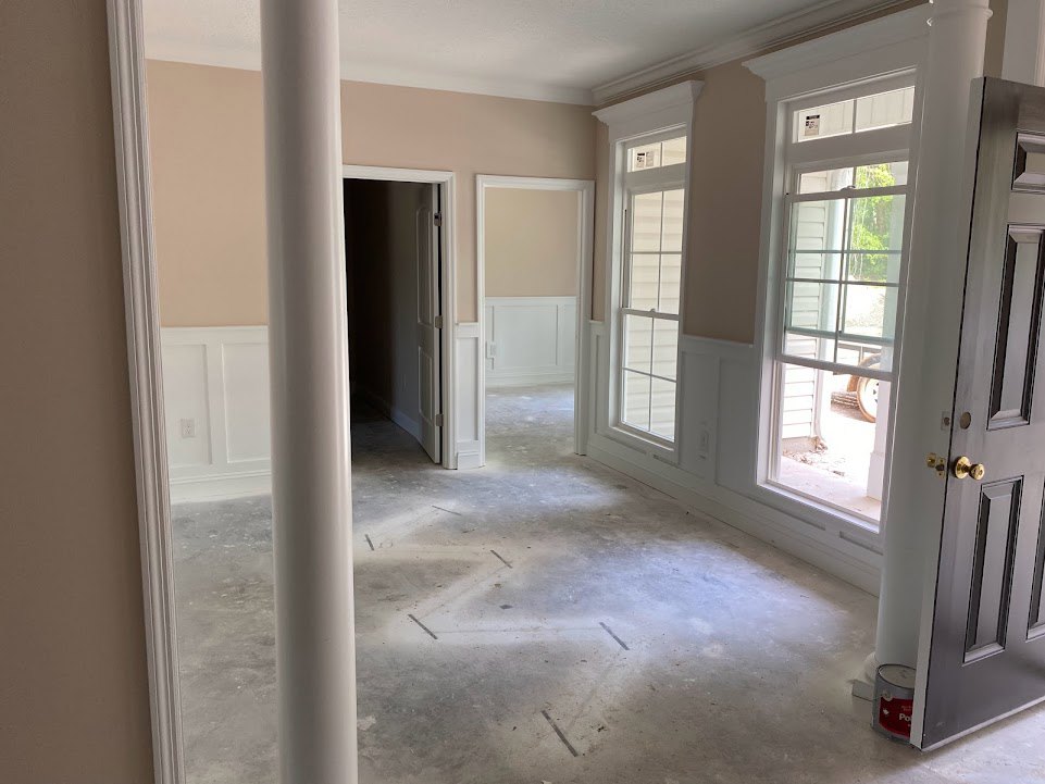 Hallway with white pillars, light walls, windows with white frames, paint can on floor, and white door against dark background