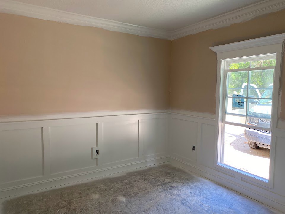 Room with white walls, square door, white ceiling molding, concrete floor with white baseboard, large window overlooking parked car outside