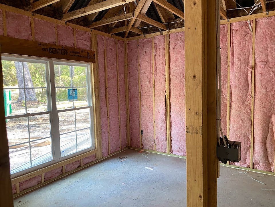 Room with exposed wooden beams, wall insulation, and a large window; visible electrical wiring and construction materials.